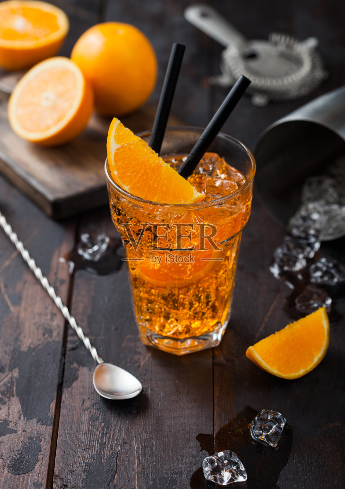 高宝杯的Spritz夏季鸡尾酒与橙片和滤网与摇酒器在深色木制背景。冰块和黑吸管。照片摄影图片