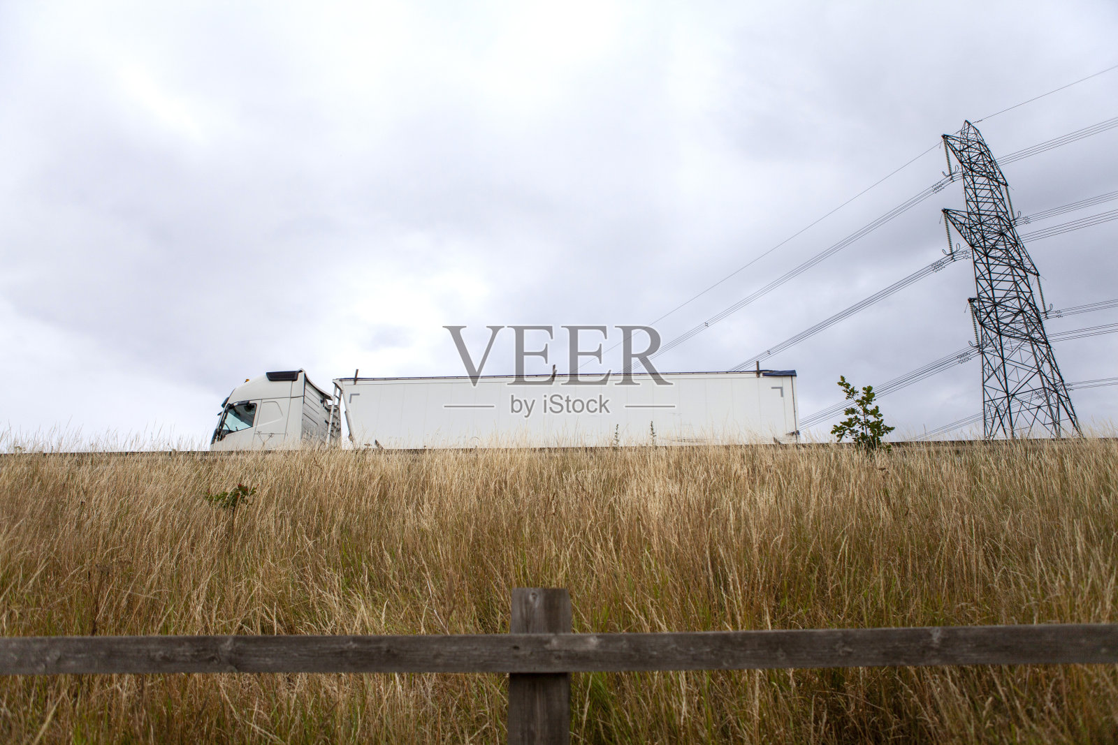 从草地脚下的路堤上看到一辆卡车经过天空阴云密布的塔架照片摄影图片