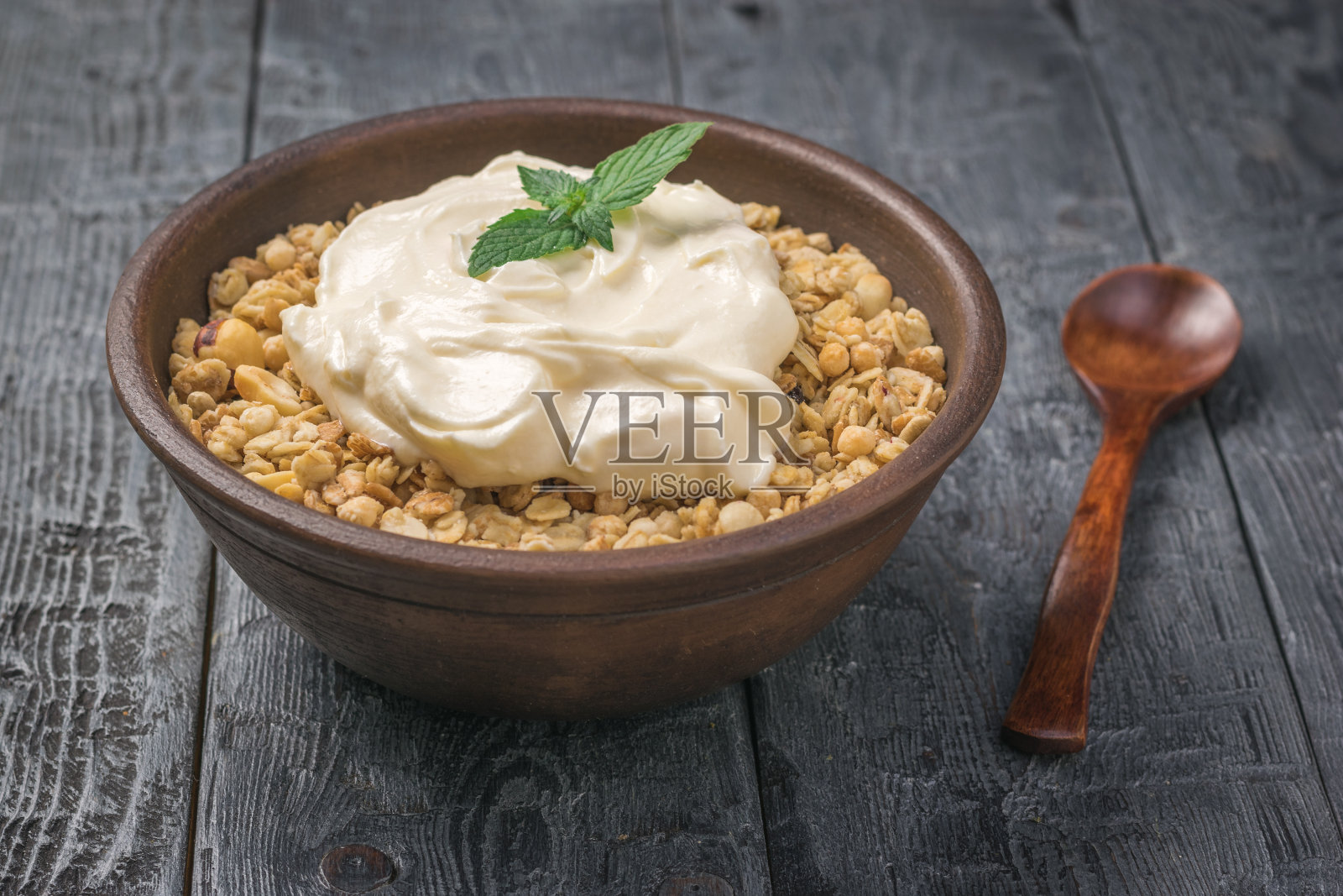 格兰诺拉麦片和酸奶放在一个粘土碗里,放在一张质朴的桌子上。照片摄影图片