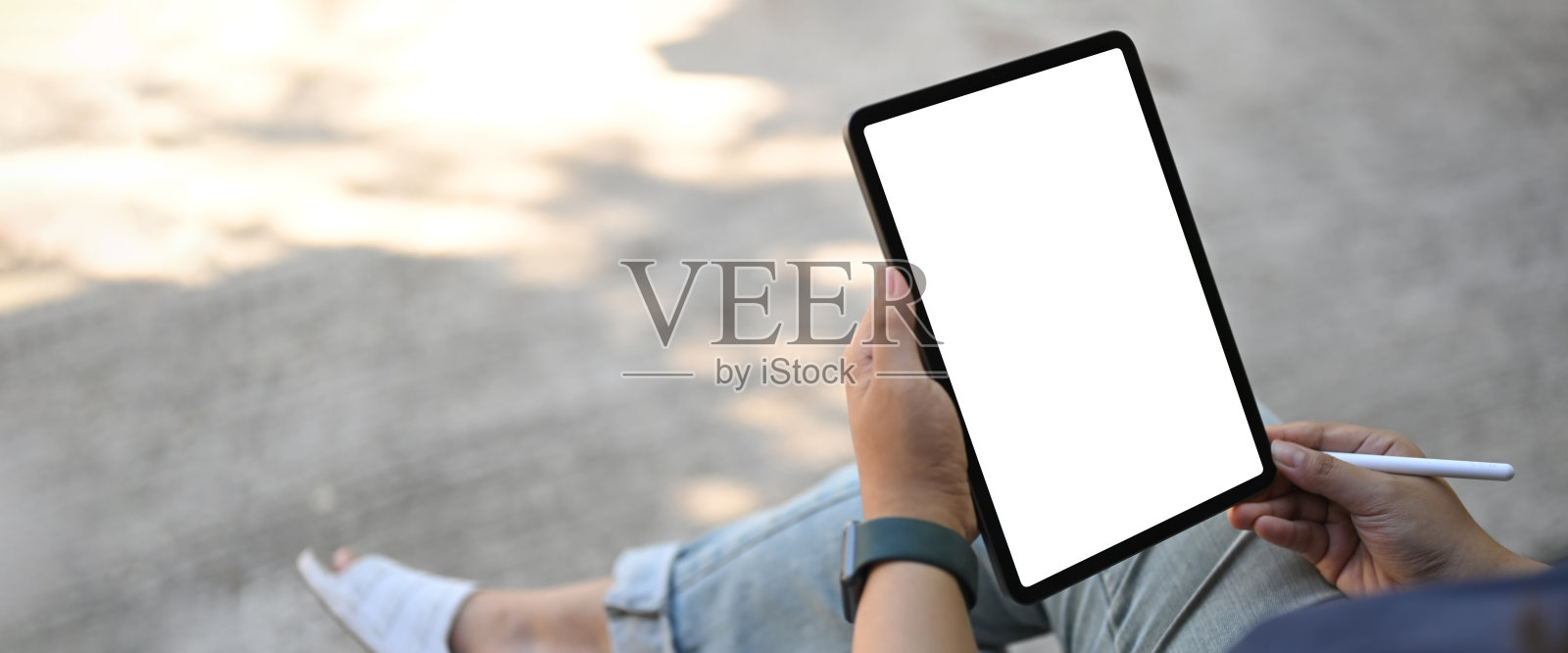 裁剪图像的手是使用一个白色空白屏幕的电脑平板电脑和手写笔在外面的家。照片摄影图片