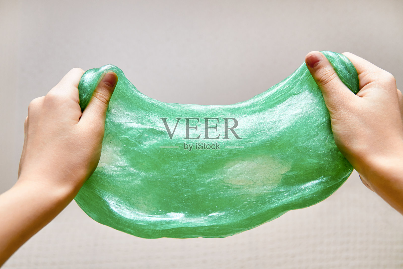 双手在浅色的背景上伸展着绿色的粘液。反应力的玩具。玩具用于发展手的运动技能。特写镜头,有选择性的重点照片摄影图片