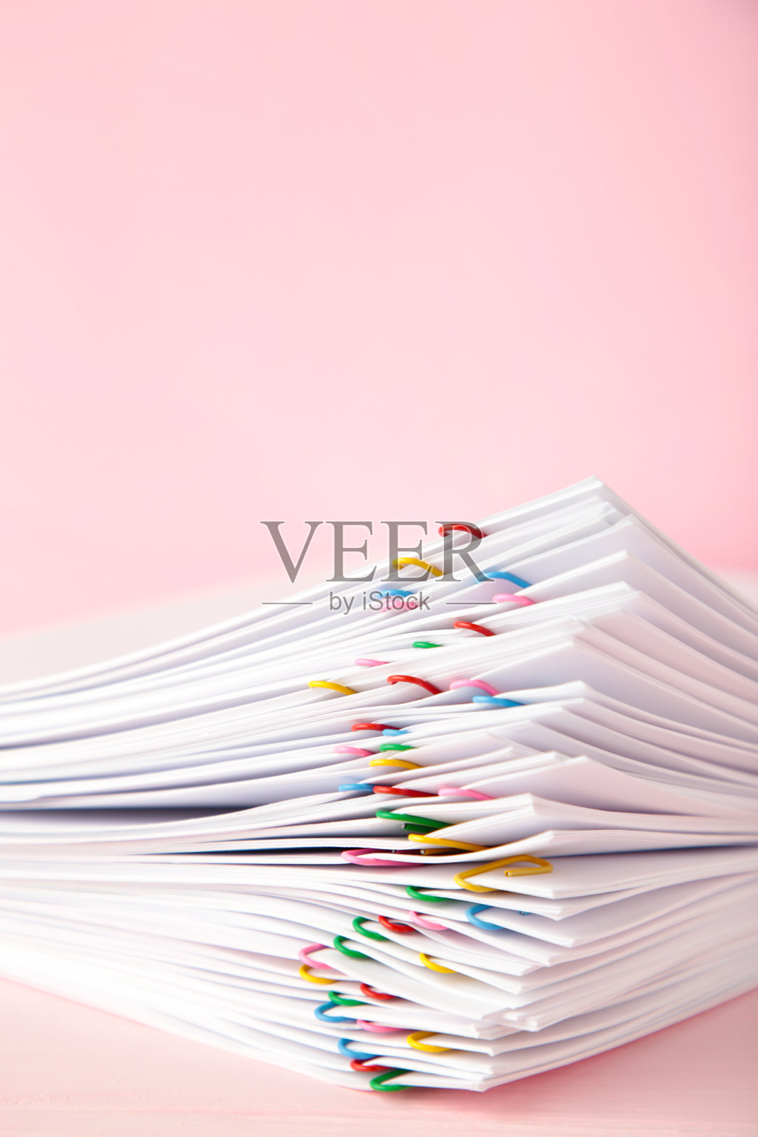 一叠白色的纸,粉色的背景上有夹子。垂直与照片摄影图片
