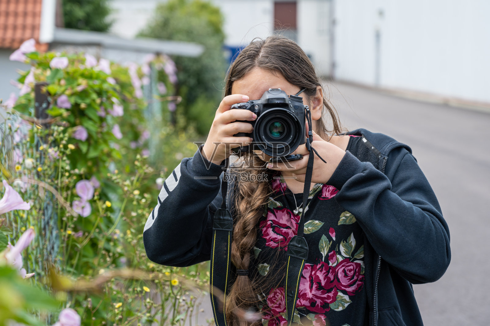 一个十多岁的小女孩正在用单反相机拍照。摄像头遮住了她的脸。模糊的,软的背景照片摄影图片