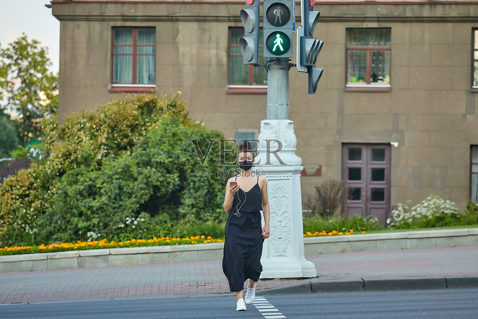 美丽的女孩戴着面具,在城市里摆姿势,拿着智能手机,用耳机听音乐照片摄影图片