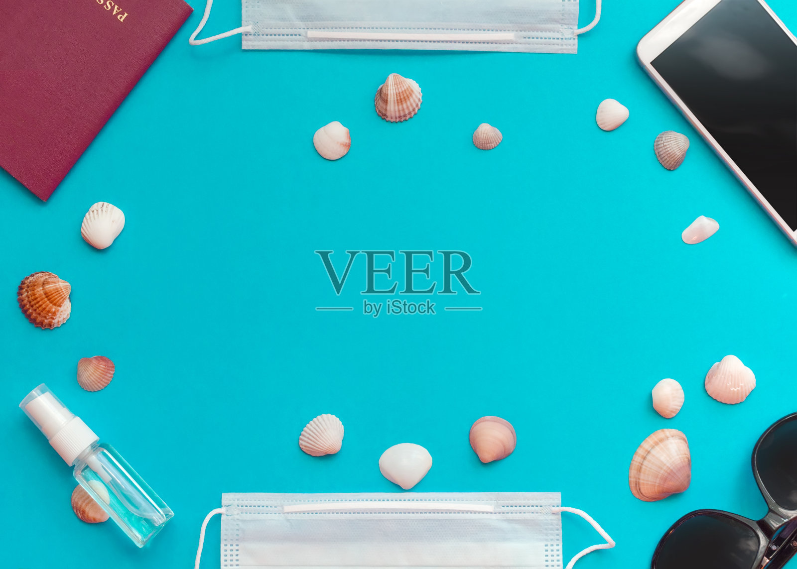 护照、手机、带防护医用口罩的太阳镜、消毒剂和贝壳在蓝色背景上。平铺和复制空间。照片摄影图片
