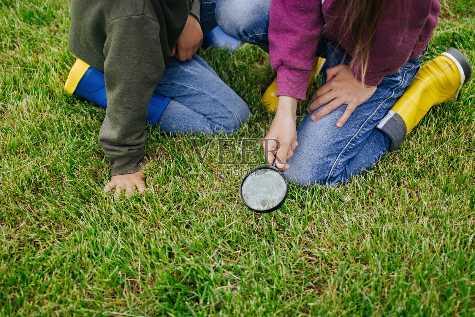 孩子们坐在绿色的草地上,用放大镜看东西。数字排毒的概念。离线的概念。与自然重新连接的概念。技术独立性。健康的休息照片摄影图片