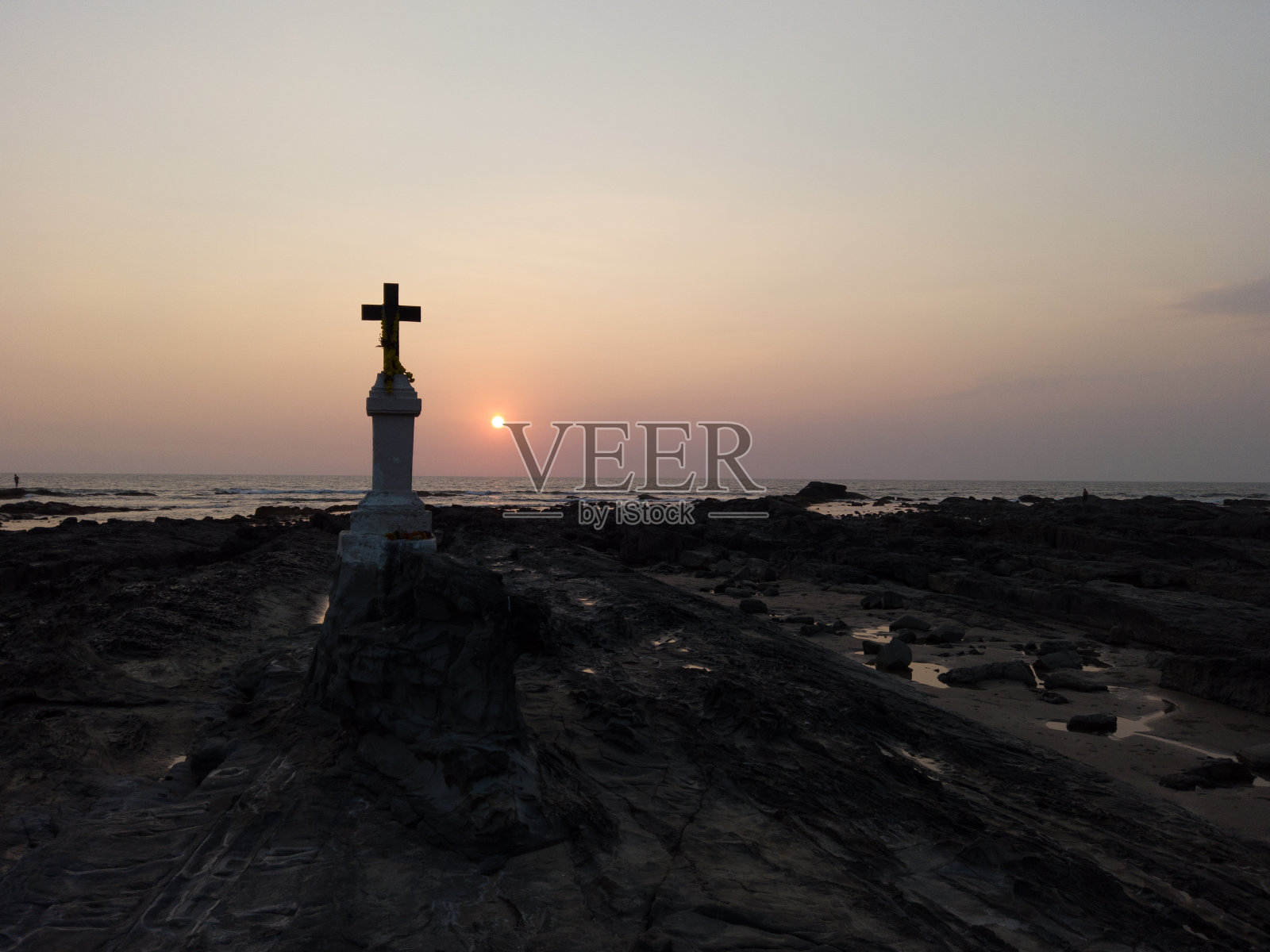 在日落的映衬下,在海边岩石上的基督十字架照片摄影图片