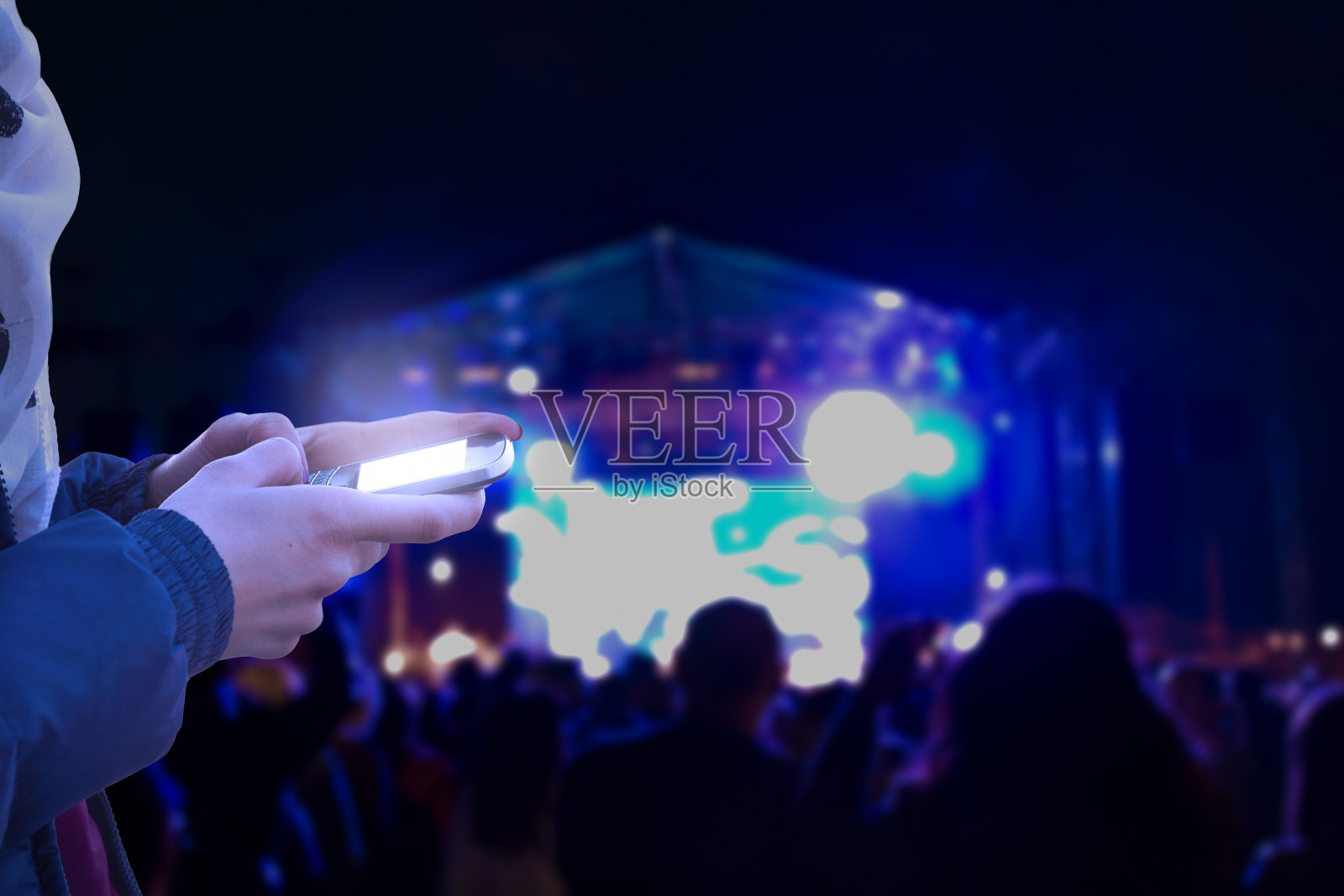 一名女子在晚上使用现代智能手机,背景是模糊的音乐会灯光。照片摄影图片