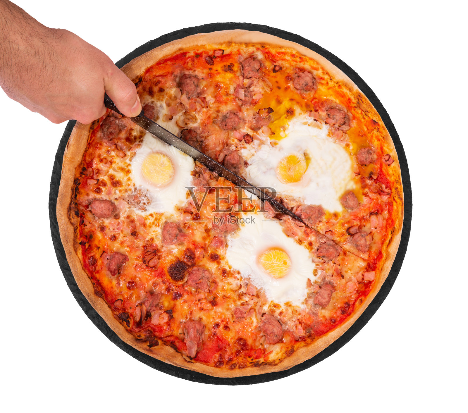 厨师用菜刀切披萨。配有牛肉香肠、鸡蛋和培根的披萨放在盘子里,孤立地放在白色的背景上照片摄影图片