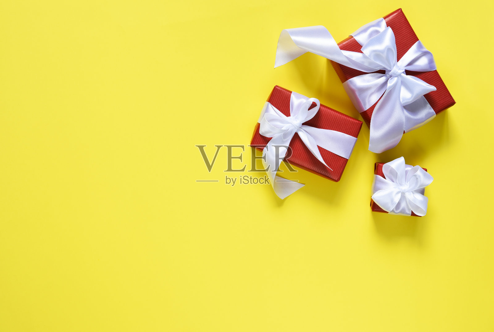 黄色背景上系着白色丝带的红盒子。“nGift盒子。前视图。布局照片摄影图片