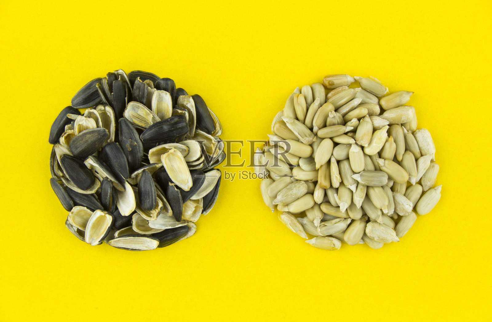 两堆烤去皮葵花籽和壳在黄色的背景。照片摄影图片