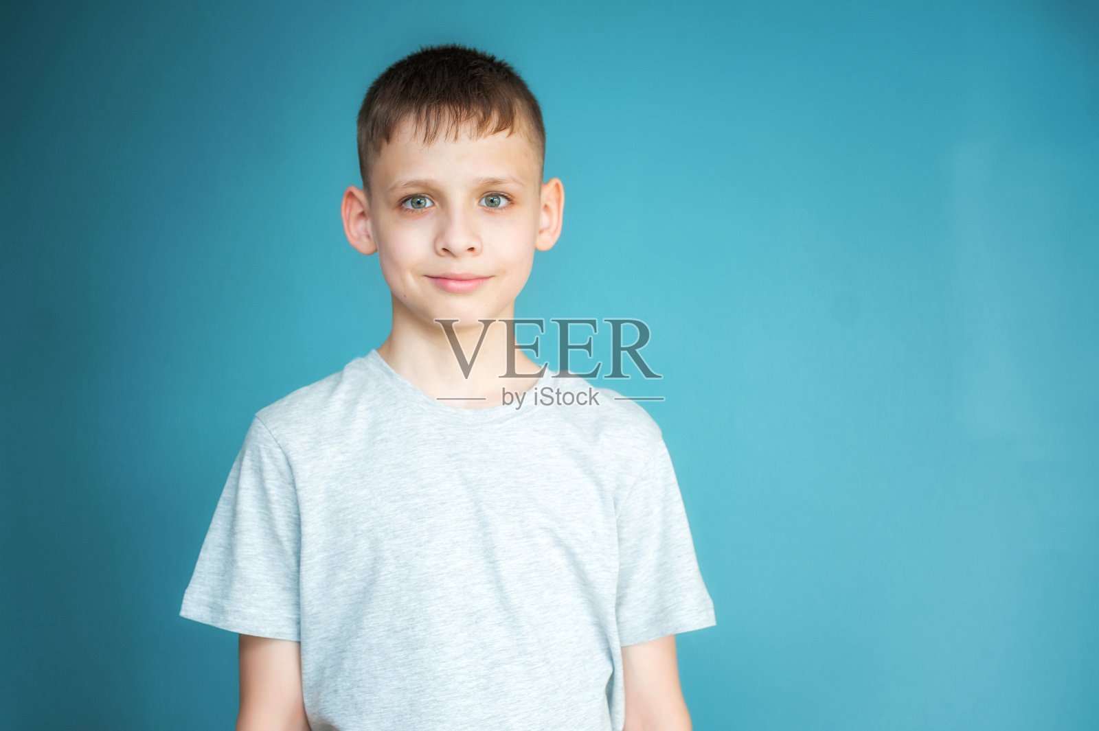 一个穿着灰色t恤的少年的肖像。蓝色背景下的小男孩的照片。他谨慎地微笑。本空间照片摄影图片
