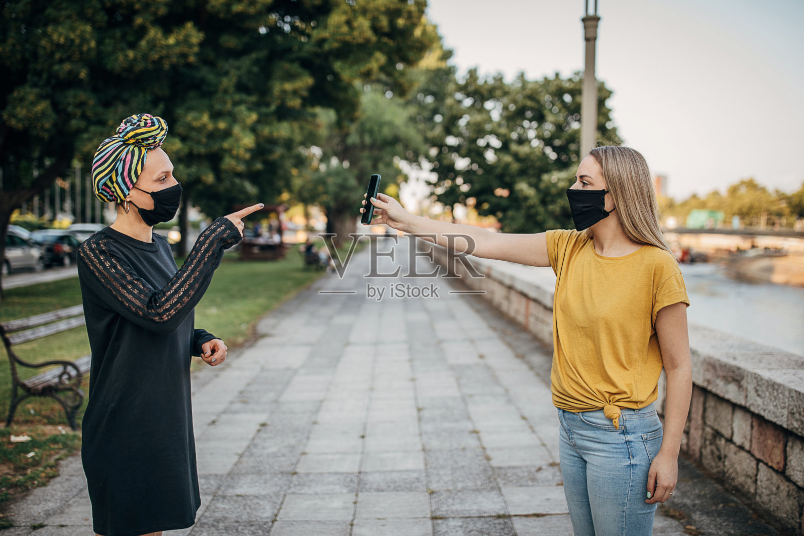 年轻女性戴着防护口罩在城市户外使用智能手机照片摄影图片