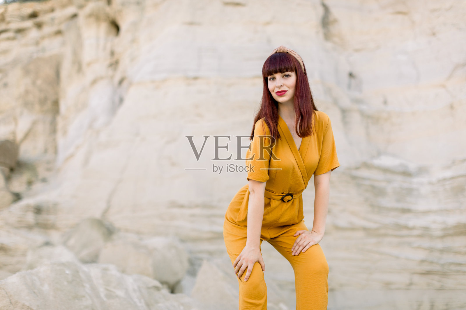 美丽的白人红头发女孩的肖像在明亮的黄色工装裤,摆姿势对着摄像机在采石场。夏季生活方式和时尚概念照片摄影图片