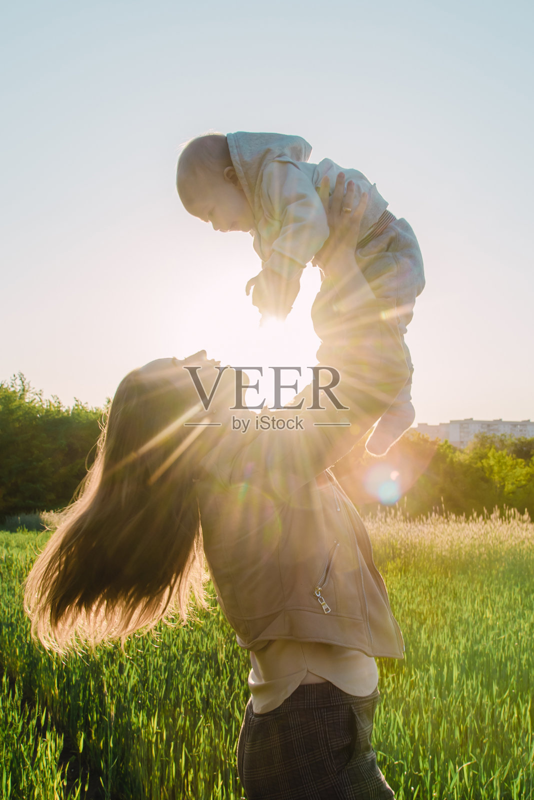 在阳光明媚的日落时分,快乐的女人抱着她的宝宝并将他抛向空中照片摄影图片