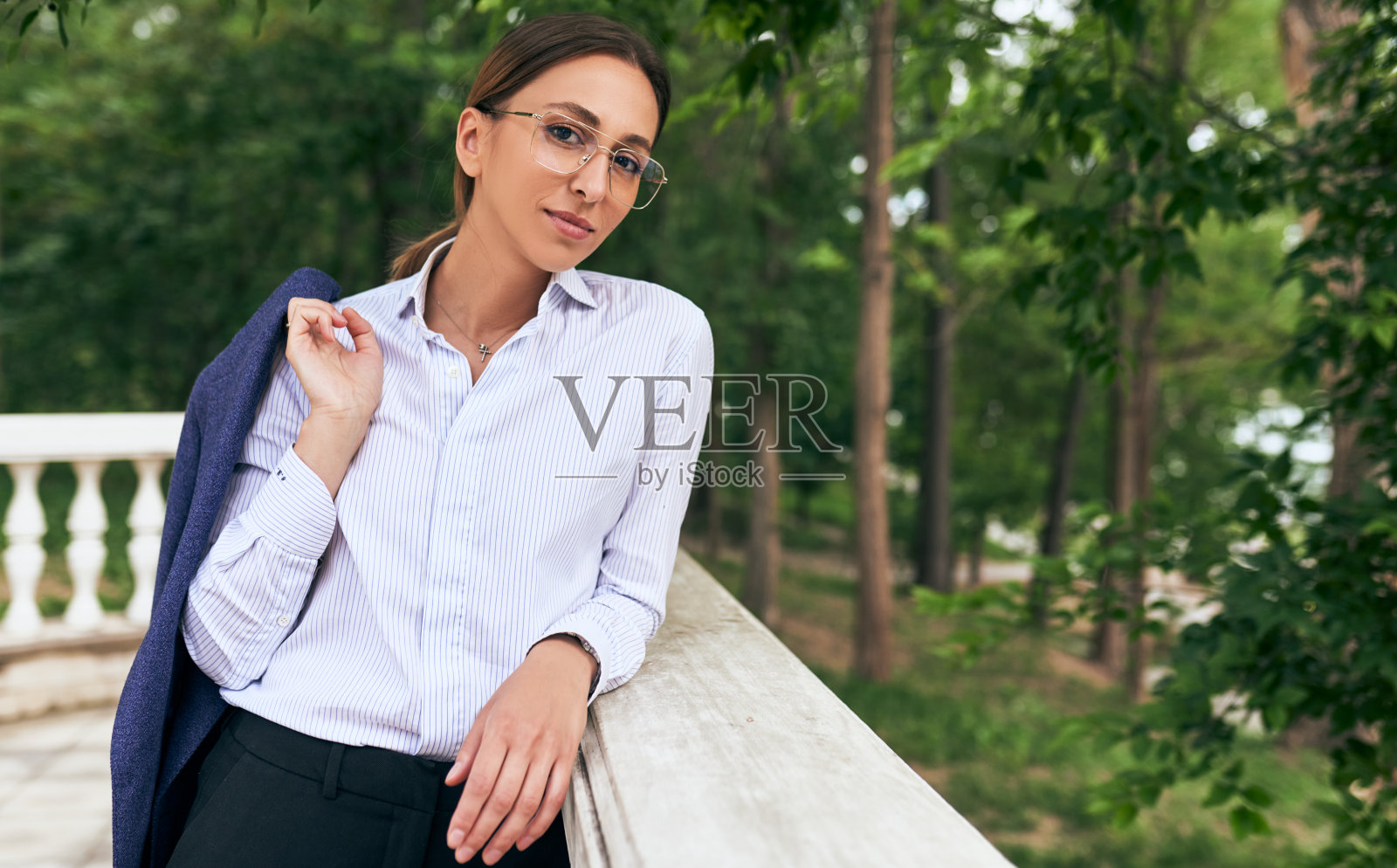 一名女企业家下班后穿着白衬衫,戴着透明眼镜在公园休息的半身肖像。成功的女商人微笑着透过眼镜看着镜头。照片摄影图片