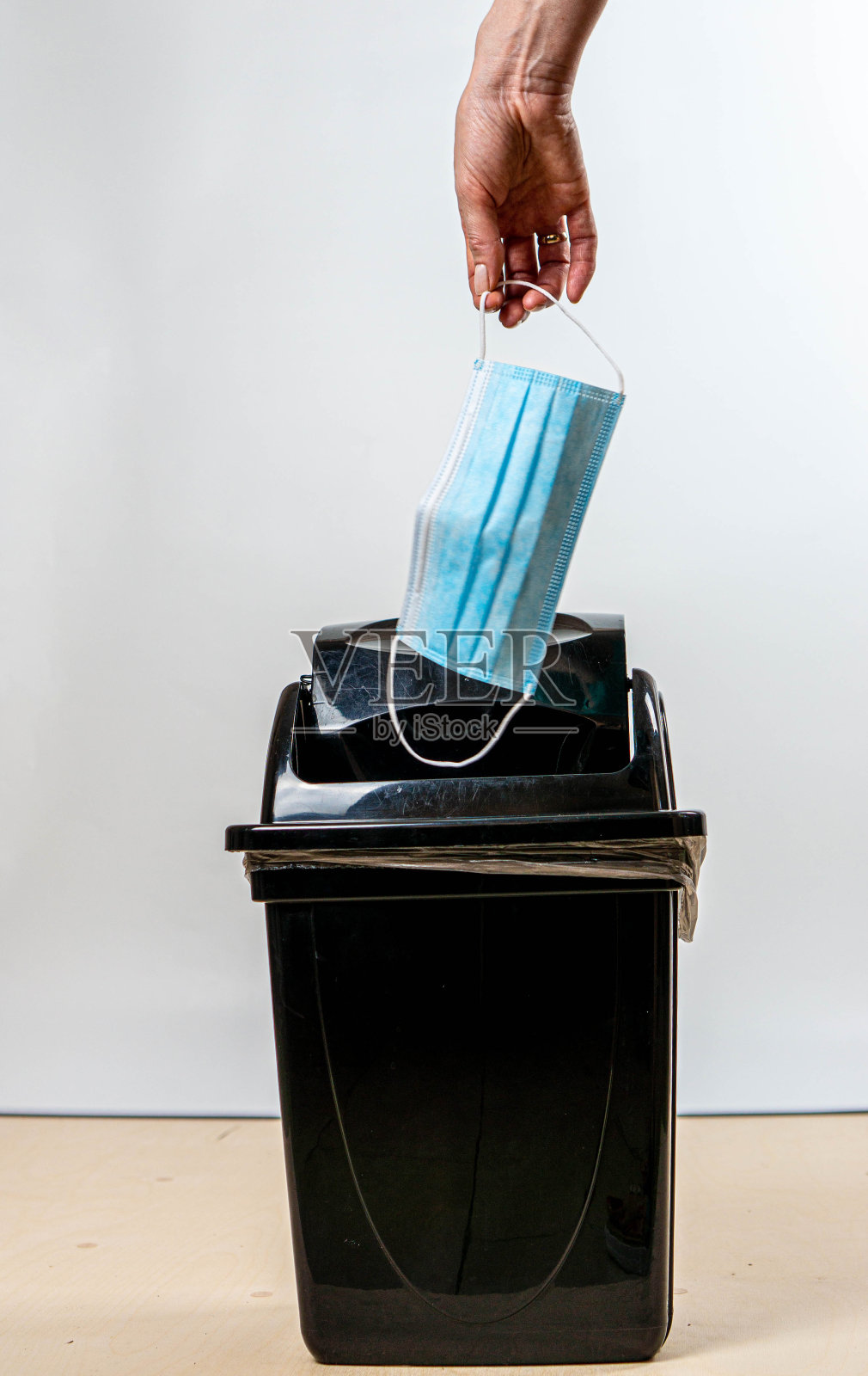 女子手将医用口罩扔进垃圾桶。白色背景。照片摄影图片