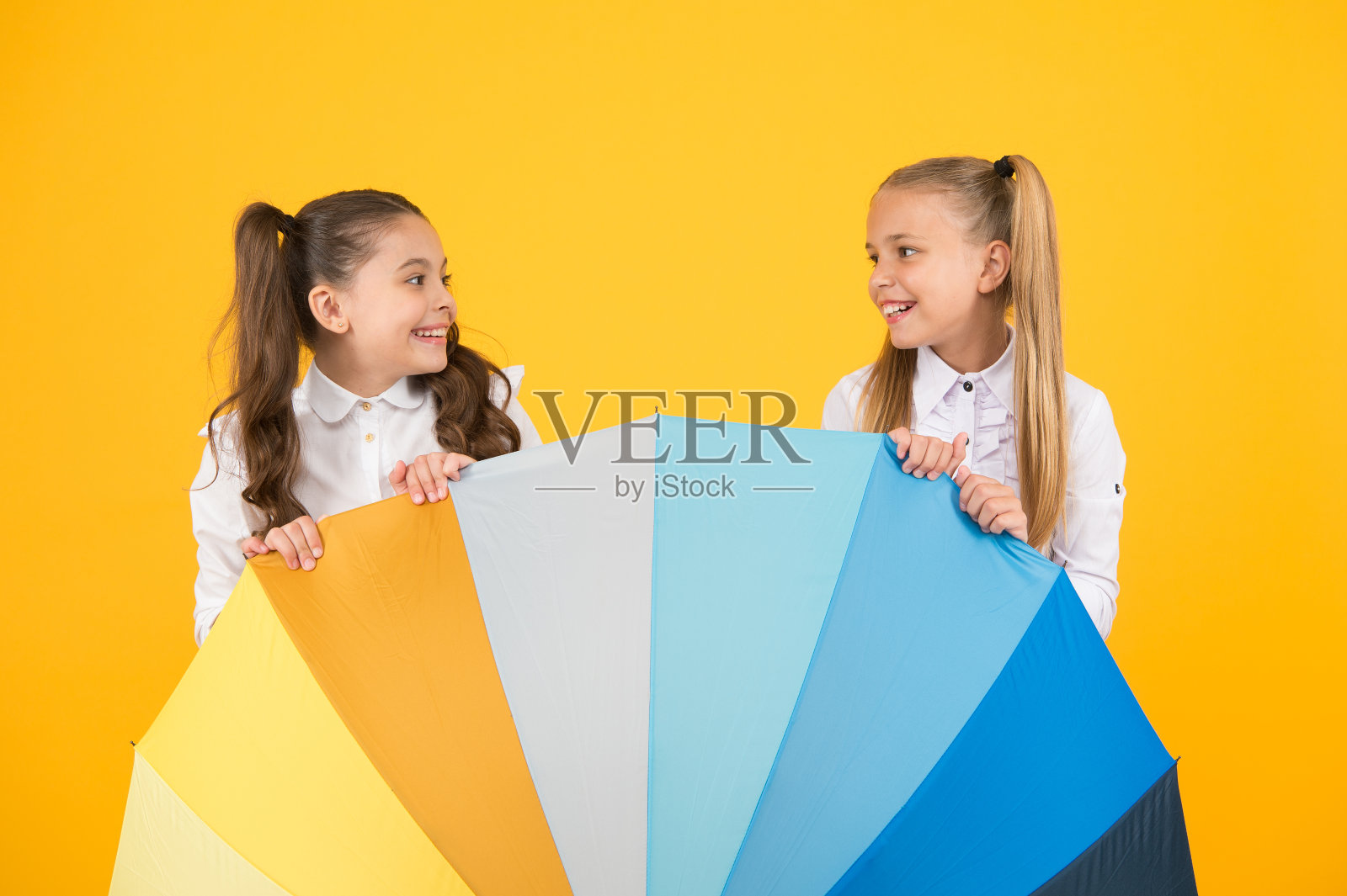 雨消失。小女生们在鲜艳的雨伞后面微笑。黄色的背景下,快乐的孩子们在雨中步行上学。阳光和雨水才能形成彩虹照片摄影图片