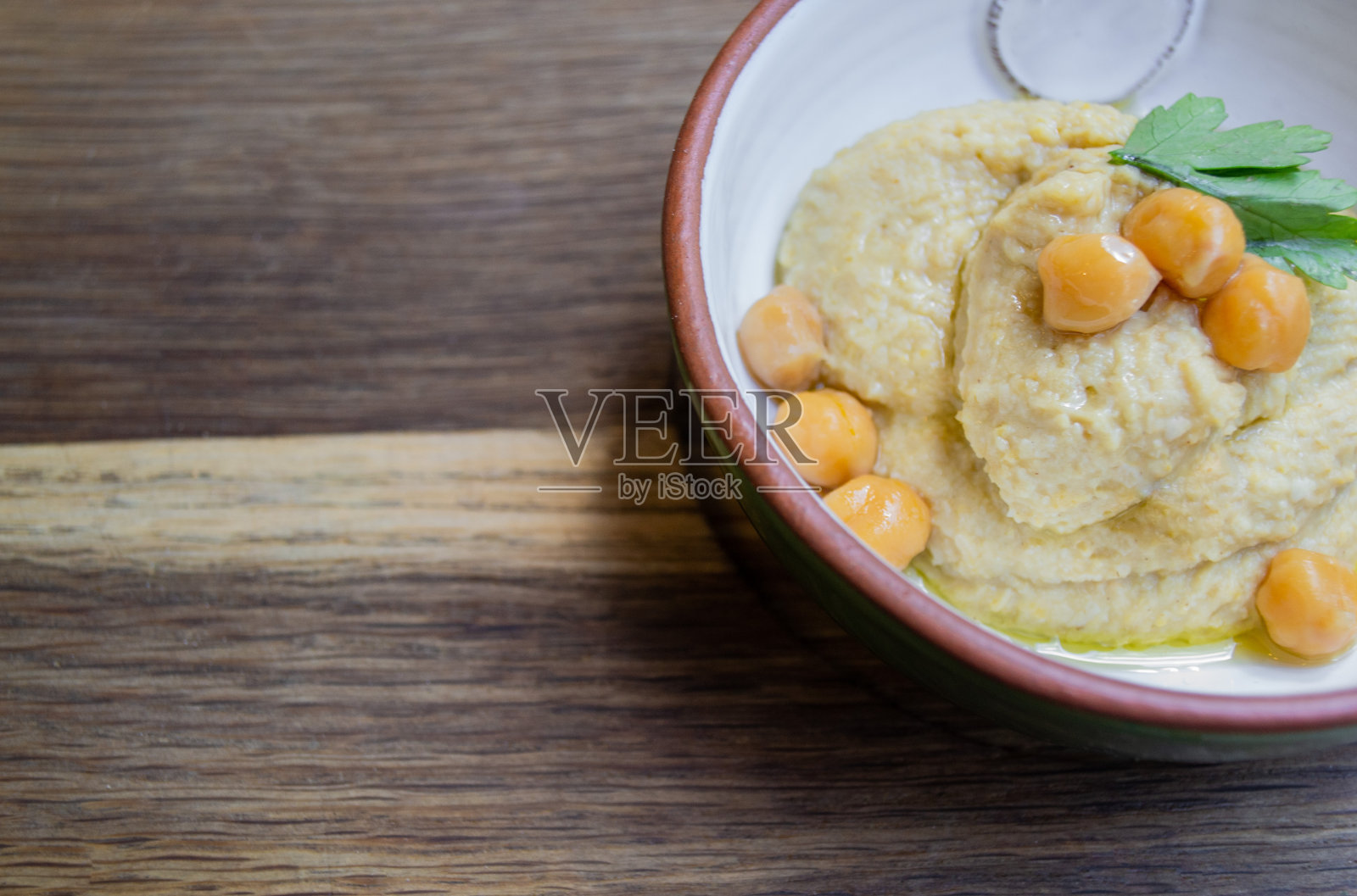 用欧芹和鹰嘴豆装饰的鹰嘴豆泥放在一个陶瓷碗里,木质背景。本空间照片摄影图片