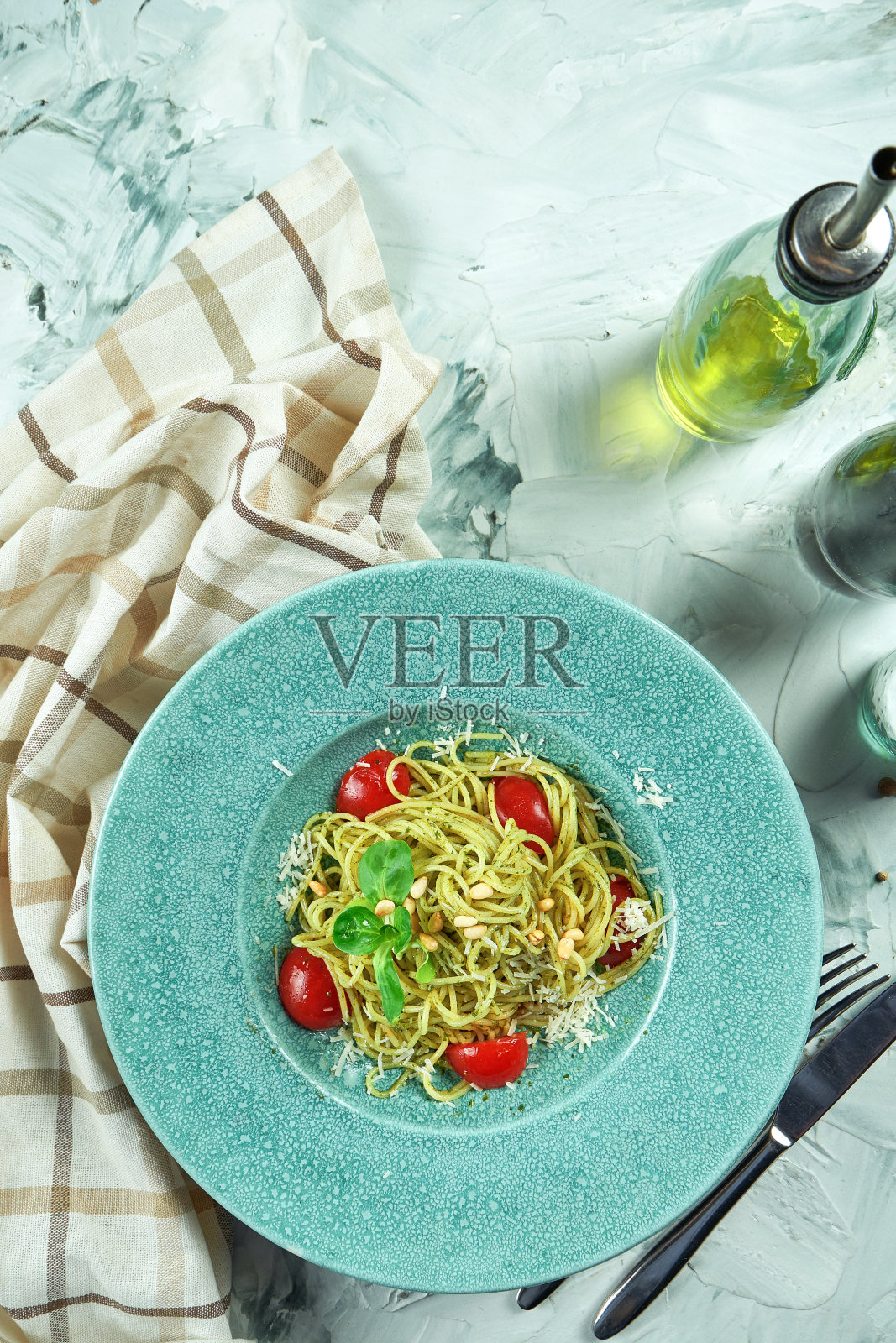 意大利意面与香蒜沙司和番茄在一个蓝色的盘子里与厨房用具组成照片摄影图片