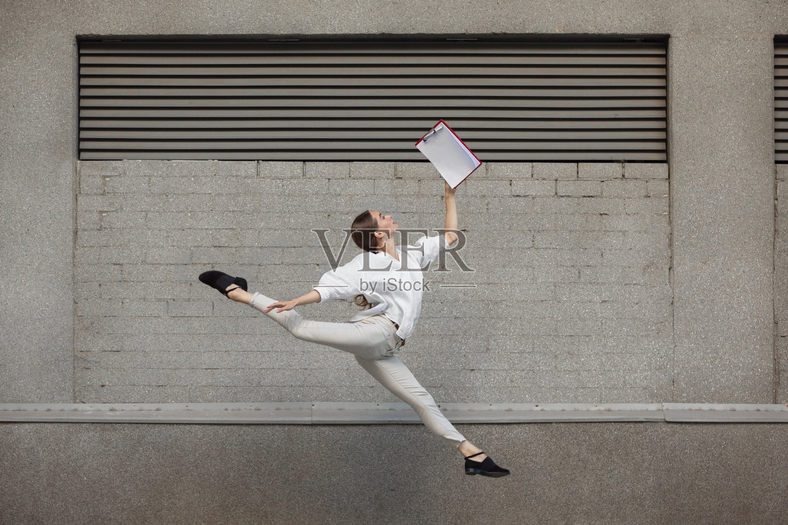 年轻女子在楼前跳跃,在奔跑中跳得很高照片摄影图片