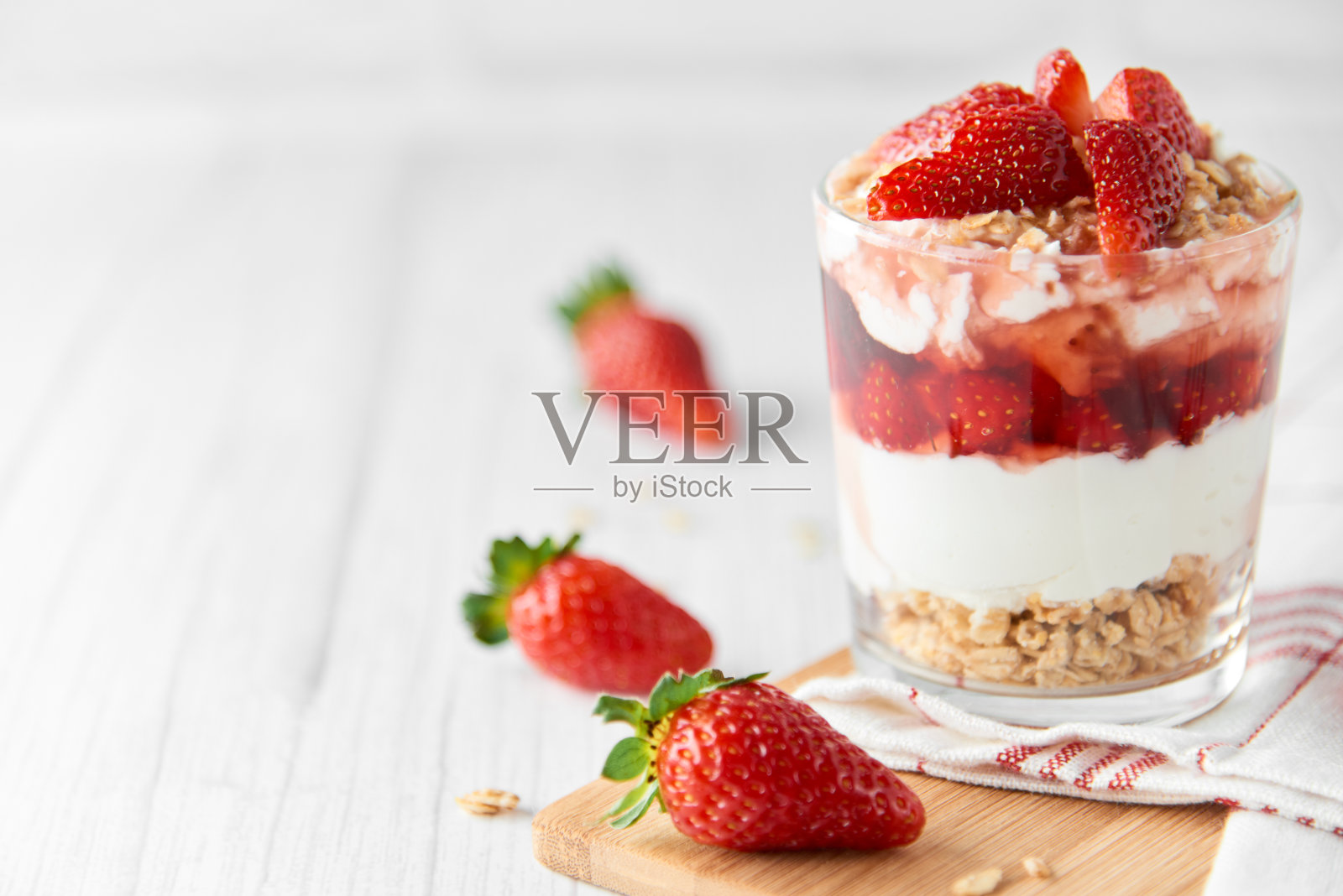 自制的分层甜点与新鲜的草莓,奶油奶酪或酸奶,格兰诺拉麦片和草莓果酱在玻璃上白木背景。健康有机早餐或零食的概念。有选择性的重点。照片摄影图片