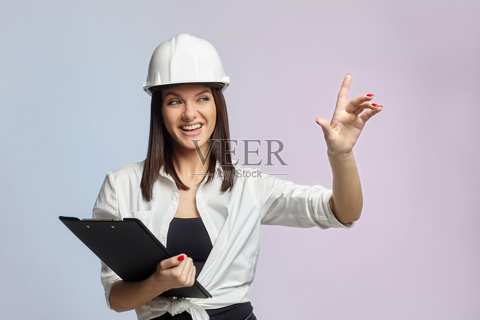 戴着白色头盔,拿着文件夹的建筑女孩。一个懂建筑、维修和现代化的女商人的概念。照片摄影图片