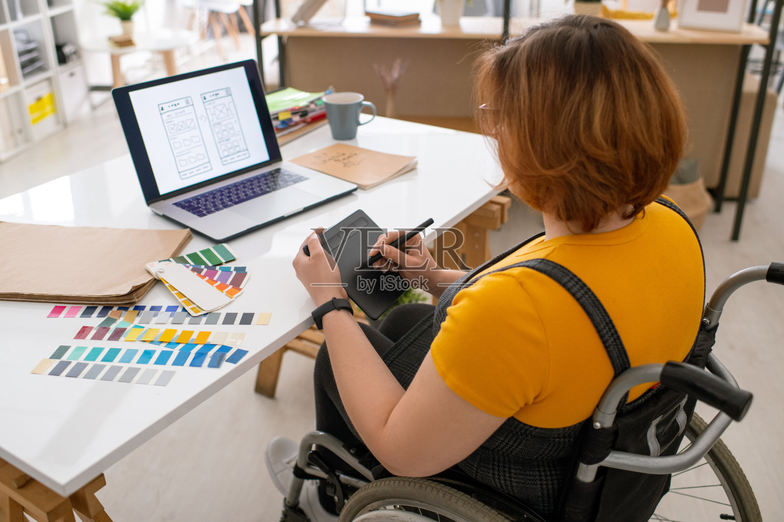 年轻的当代设计师在轮椅上使用平板电脑与手写笔工作照片摄影图片