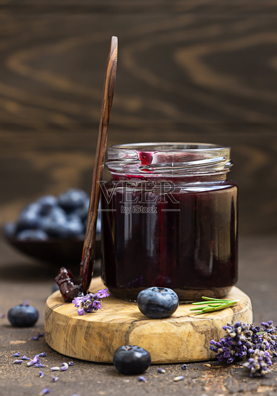 玻璃罐和勺子,美味的蓝莓果酱,新鲜的浆果,薰衣草和迷迭香在深棕色的桌子。健康的早餐。照片摄影图片