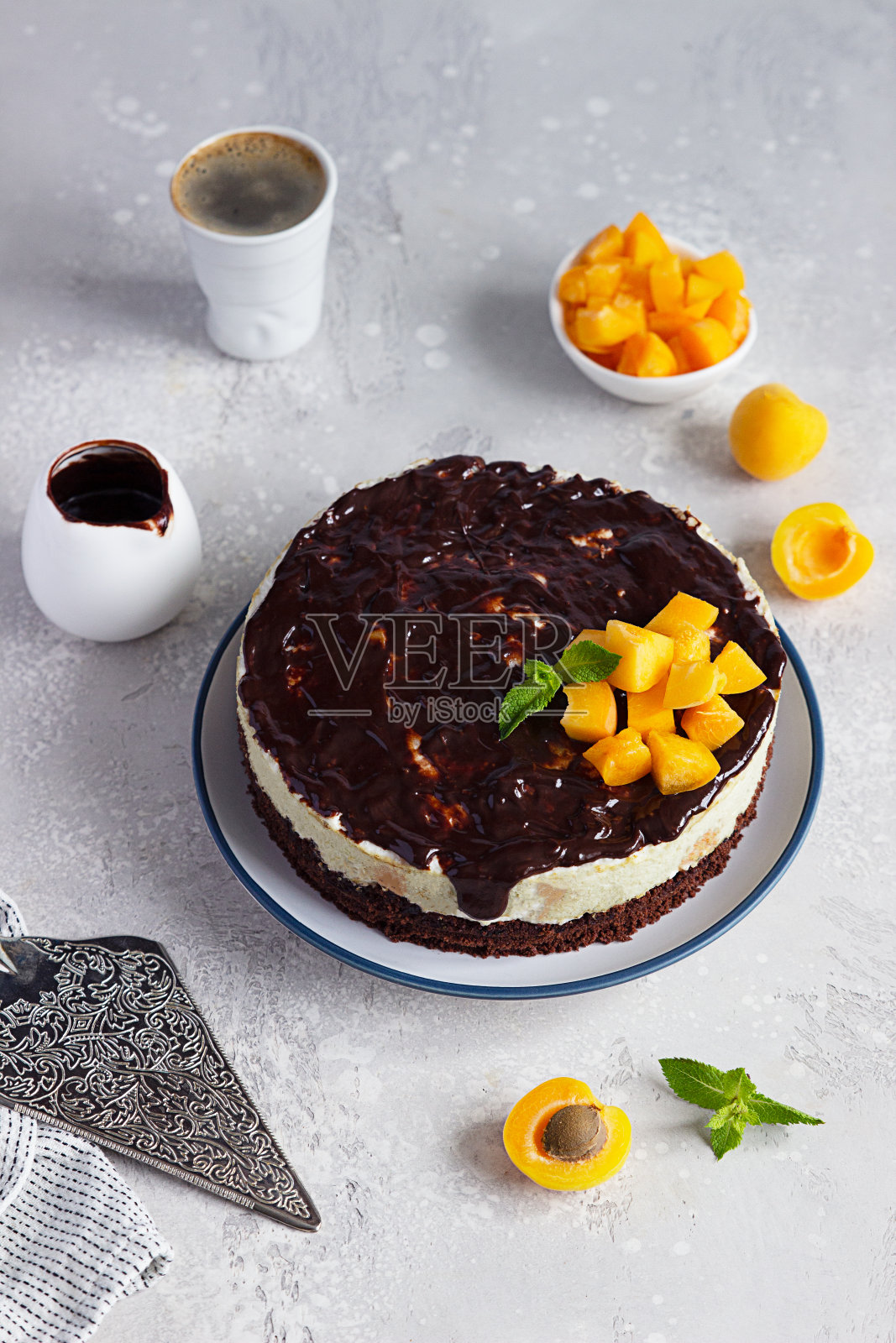 奶油慕斯蛋糕或不烤芝士蛋糕与杏子装饰巧克力釉,新鲜杏子和薄荷在明亮的背景。照片摄影图片