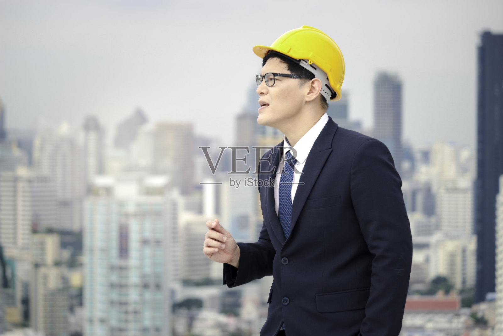 快乐的亚洲年轻商人工程师西装戴安全帽,唱歌和跳舞的屋顶与摩天大楼的城市景观照片摄影图片