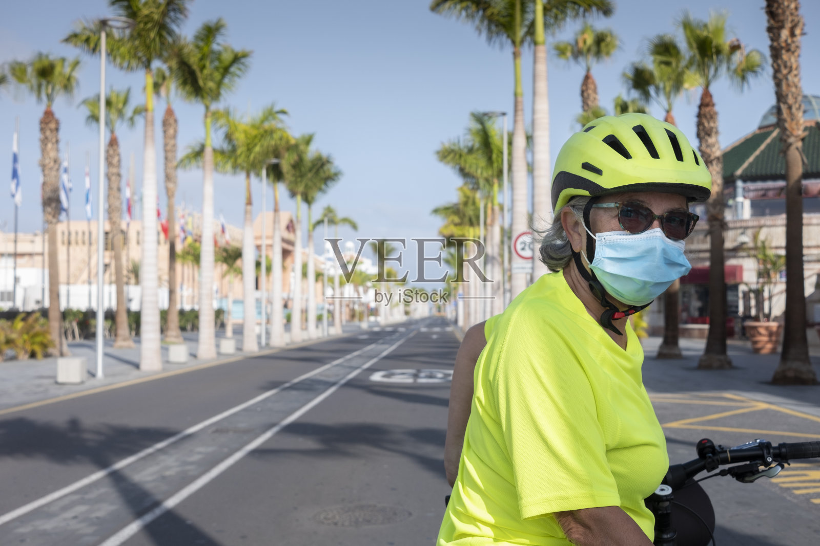 由于冠状病毒危机,一名戴着面罩、自行车和头盔的老年活跃妇女在无人问路的街道上转向,特内里费岛没有游客照片摄影图片