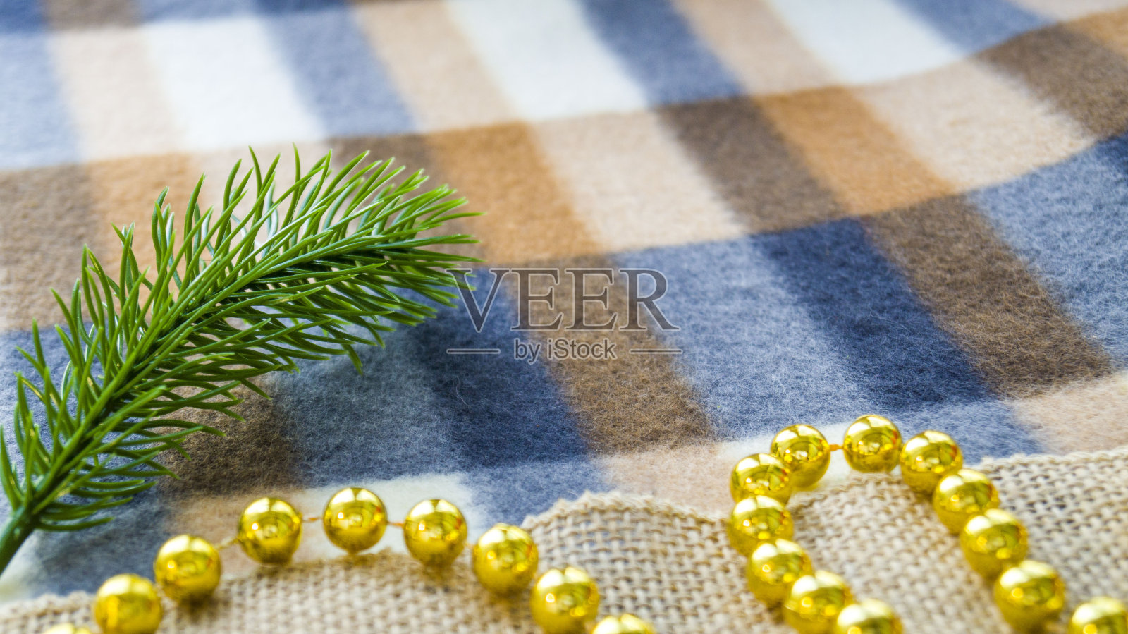 新年和圣诞贺卡。毯子上的圣诞装饰。一根云杉树枝和珠子躺在冬天的格子毯子上照片摄影图片