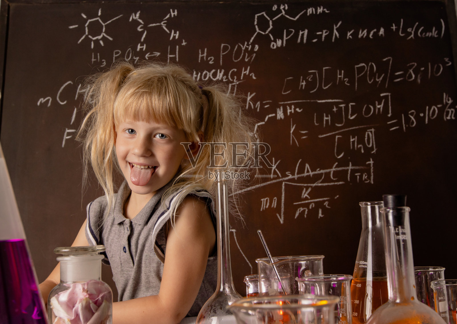 一个金发小女孩在学校实验室里拿着装有彩色物质的试管伸着她的舌头。照片摄影图片