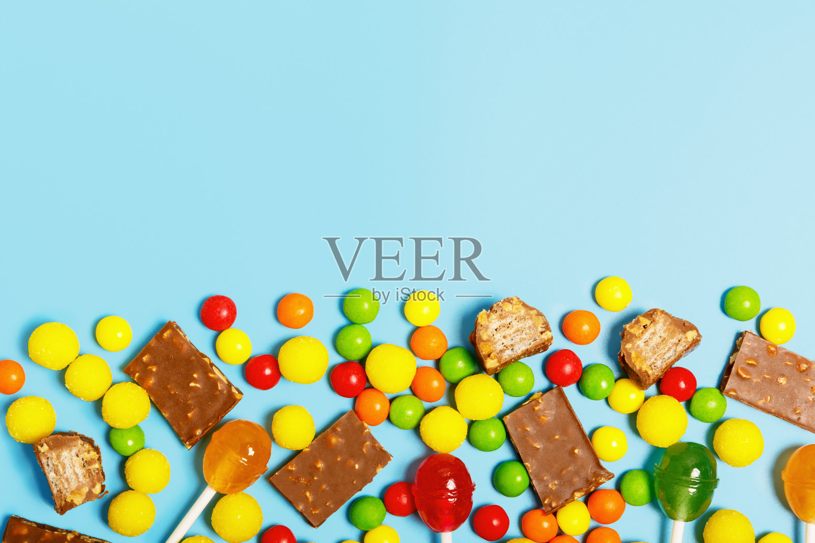 蓝色背景上的五颜六色的糖果、棒棒糖和巧克力。照片摄影图片