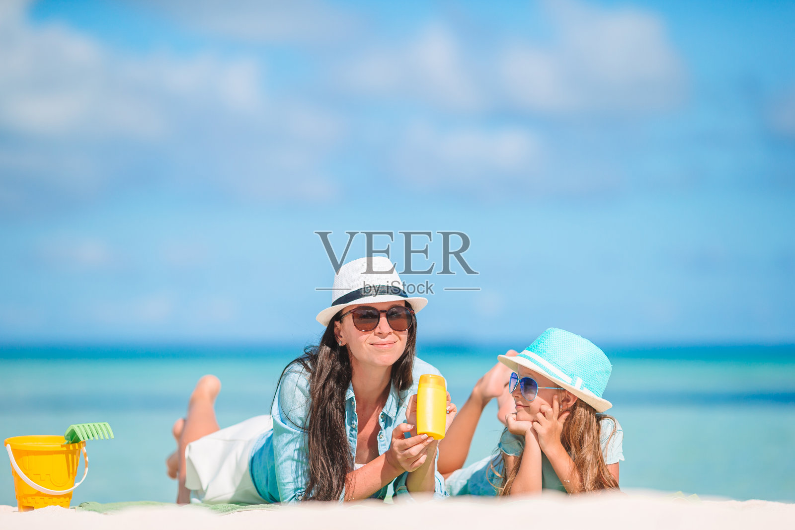 在炎热的夏天,妈妈在海滩上给小女儿涂防晒霜照片摄影图片