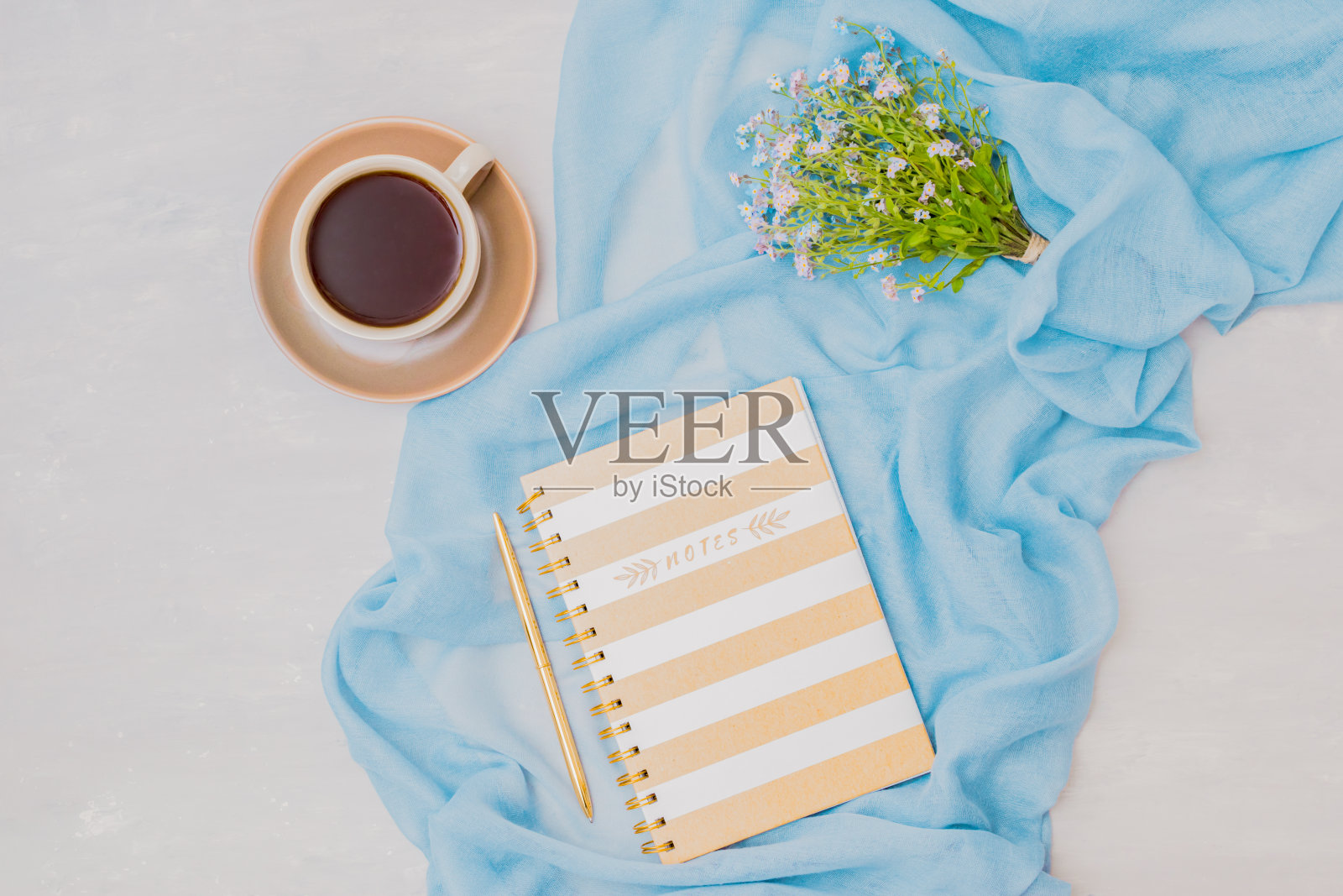 一个平面的博客或自由职业者的工作空间,一个笔记本,一杯咖啡和小的蓝色花在一个明亮的背景照片摄影图片