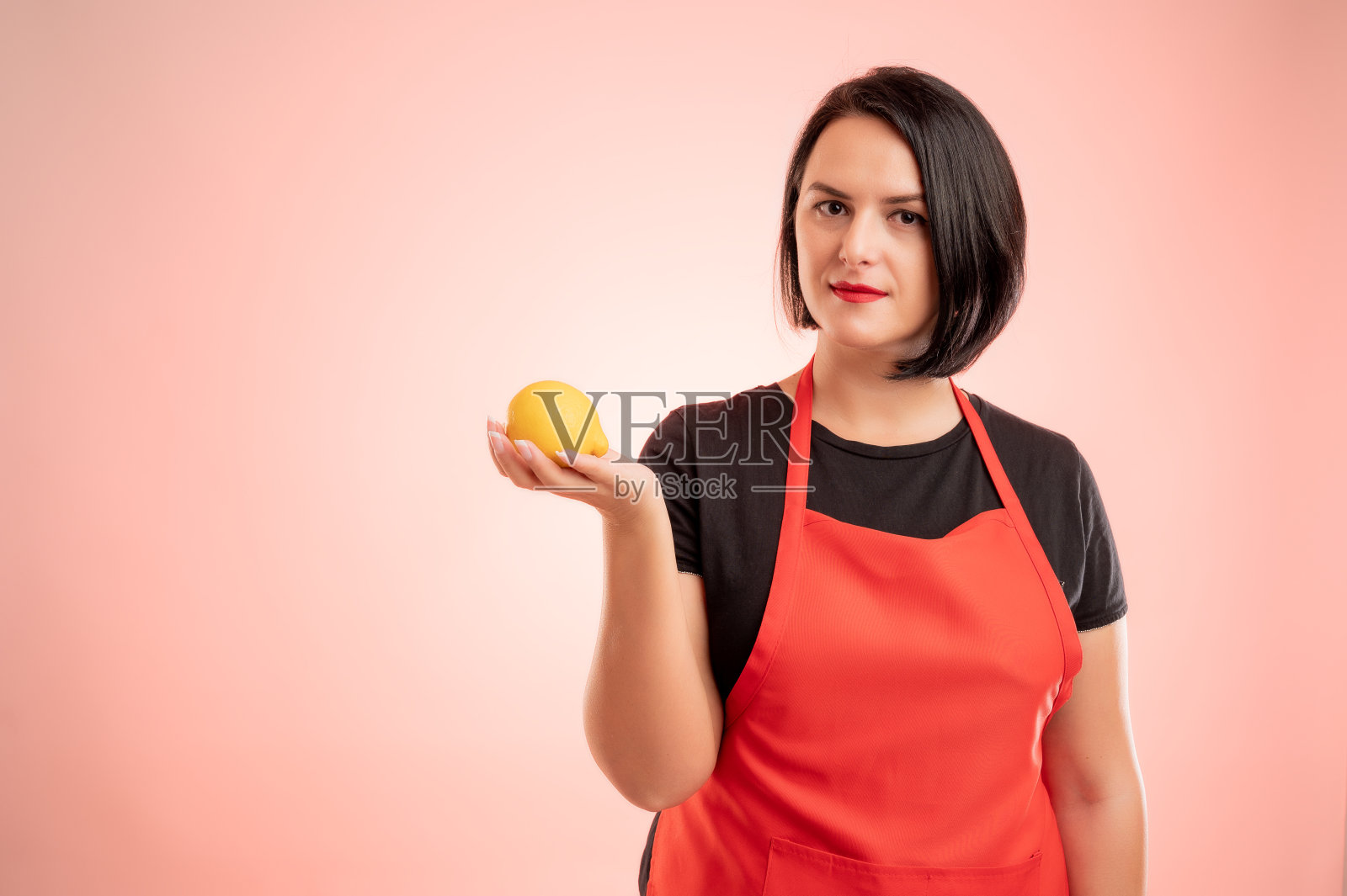 一名在超市工作的妇女,穿着红围裙和黑t恤,手里拿着一个柠檬照片摄影图片