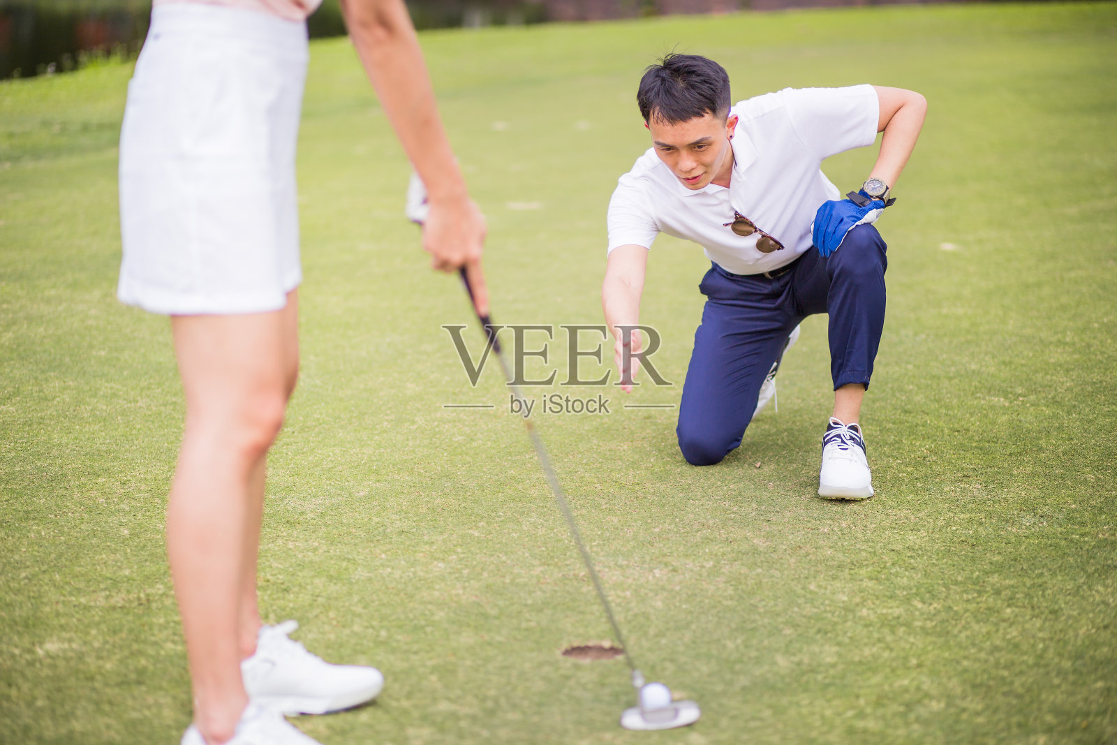 一对亚洲华人夫妇在果岭上。成熟的男人正在给他的伙伴看方向洞。照片摄影图片