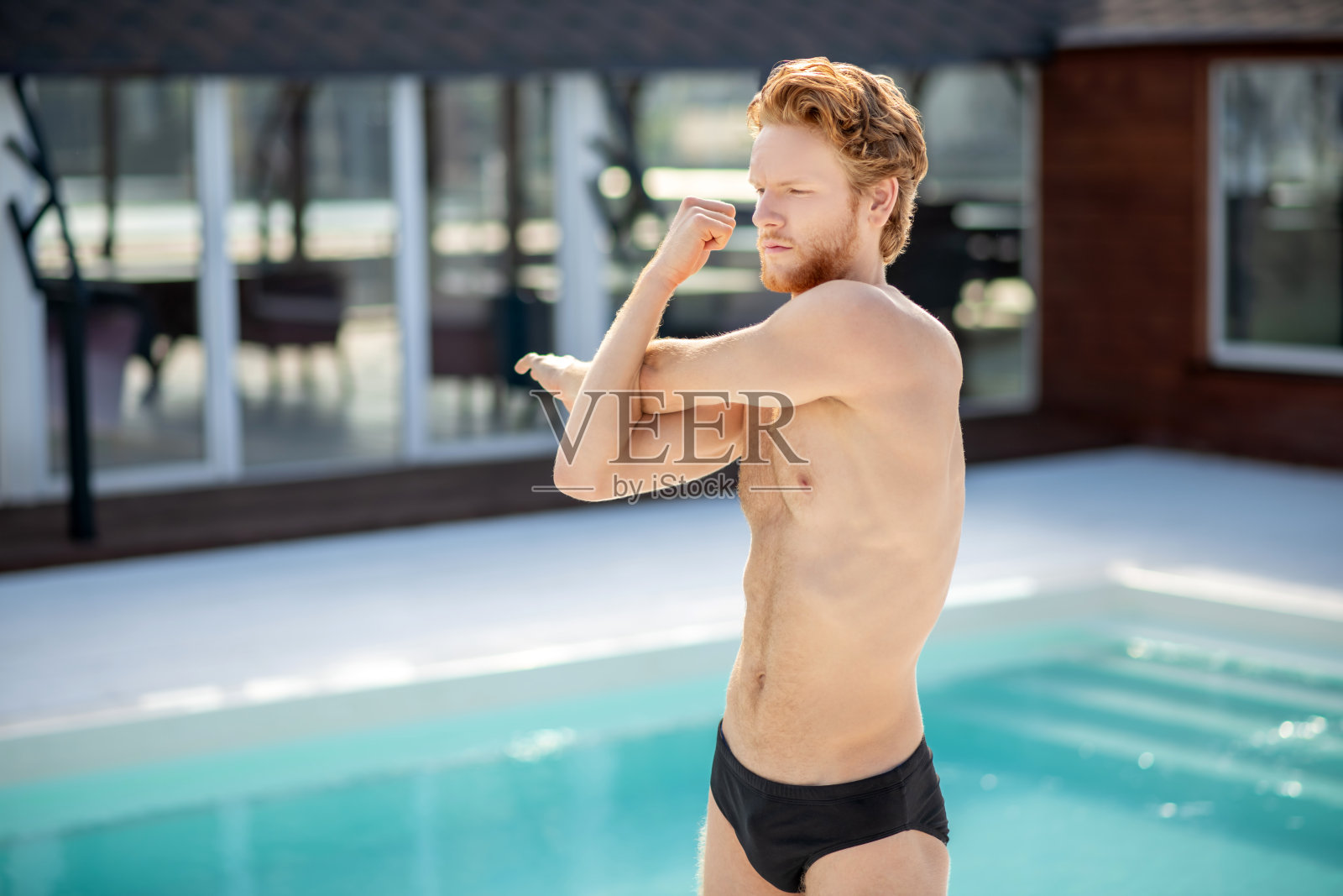 一个穿着泳衣的红发年轻人在游泳池附近照片摄影图片