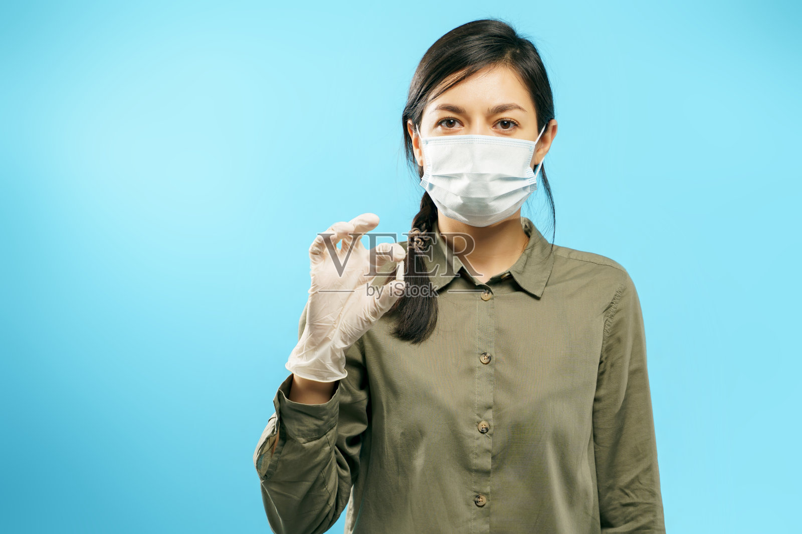 一名年轻妇女的肖像,戴着医用防护口罩和手套,拿着一个胶囊或药丸在一个蓝色的背景照片摄影图片