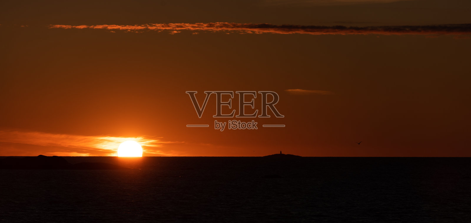 夕阳西下,海面上有小岛,地平线上有灯塔照片摄影图片