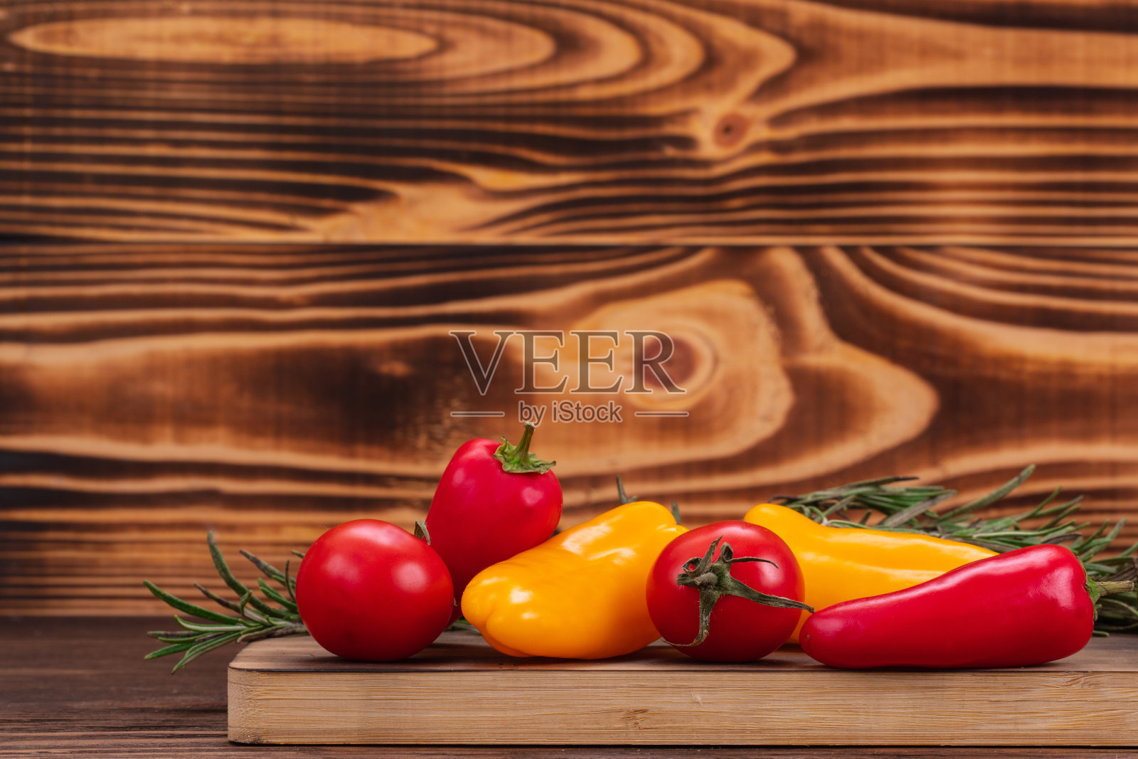 生的有机甜椒和樱桃番茄放在切菜板上,配上迷迭香嫩枝。新鲜蔬菜,健康生物食品,木质背景和复制空间照片摄影图片