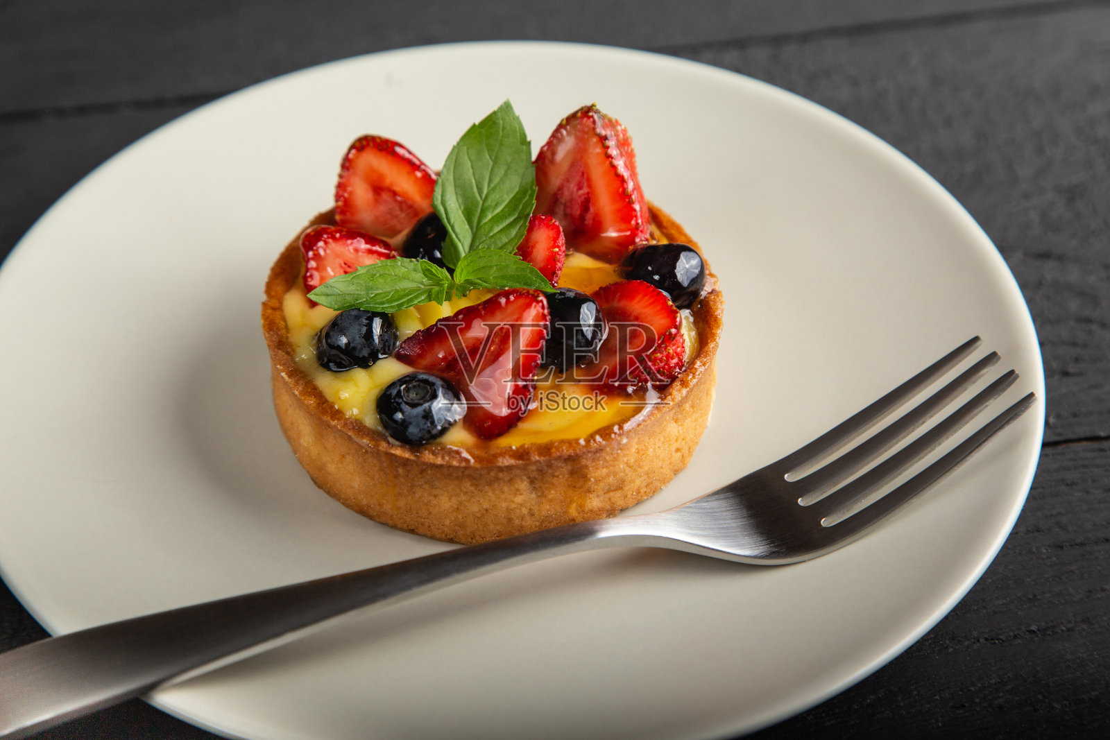 水果蛋糕与浆果,香草奶油和薄荷叶在白色盘子与叉子照片摄影图片