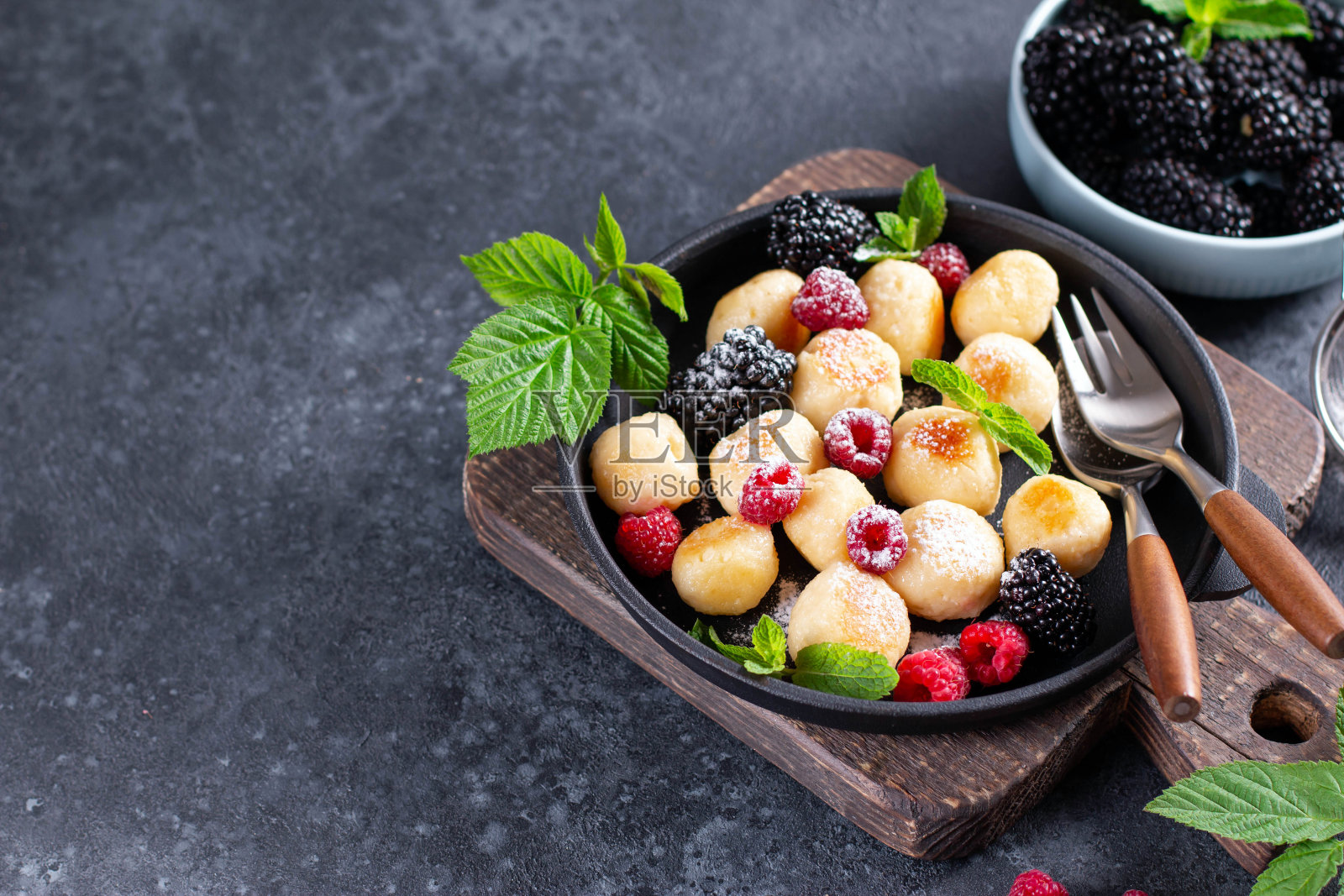 白软干酪“懒”饺子配上覆盆子、黑莓、薄荷和糖粉,放在深色的混凝土背景上。本空间照片摄影图片