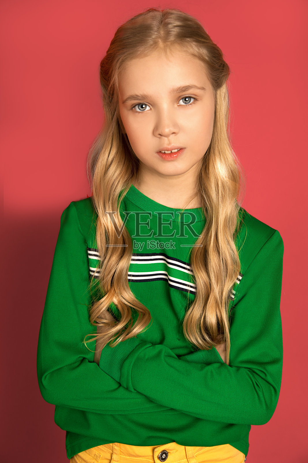 一个美丽甜美严肃的女孩,8-10岁,金发,蓝色或灰色的眼睛,卷曲的头发,鲜艳的衣服在粉红色的背景。紧急照片在工作室。特写肖像。照片摄影图片