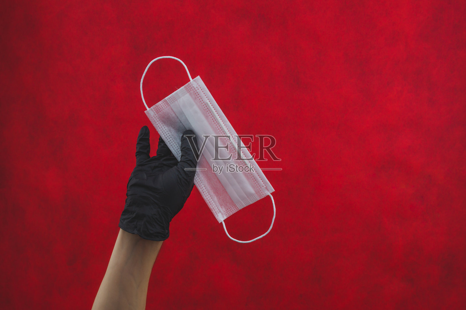 手持黑色手术手套,红色背景上手持白色医用口罩。预防呼吸道疾病和病毒的措施照片摄影图片