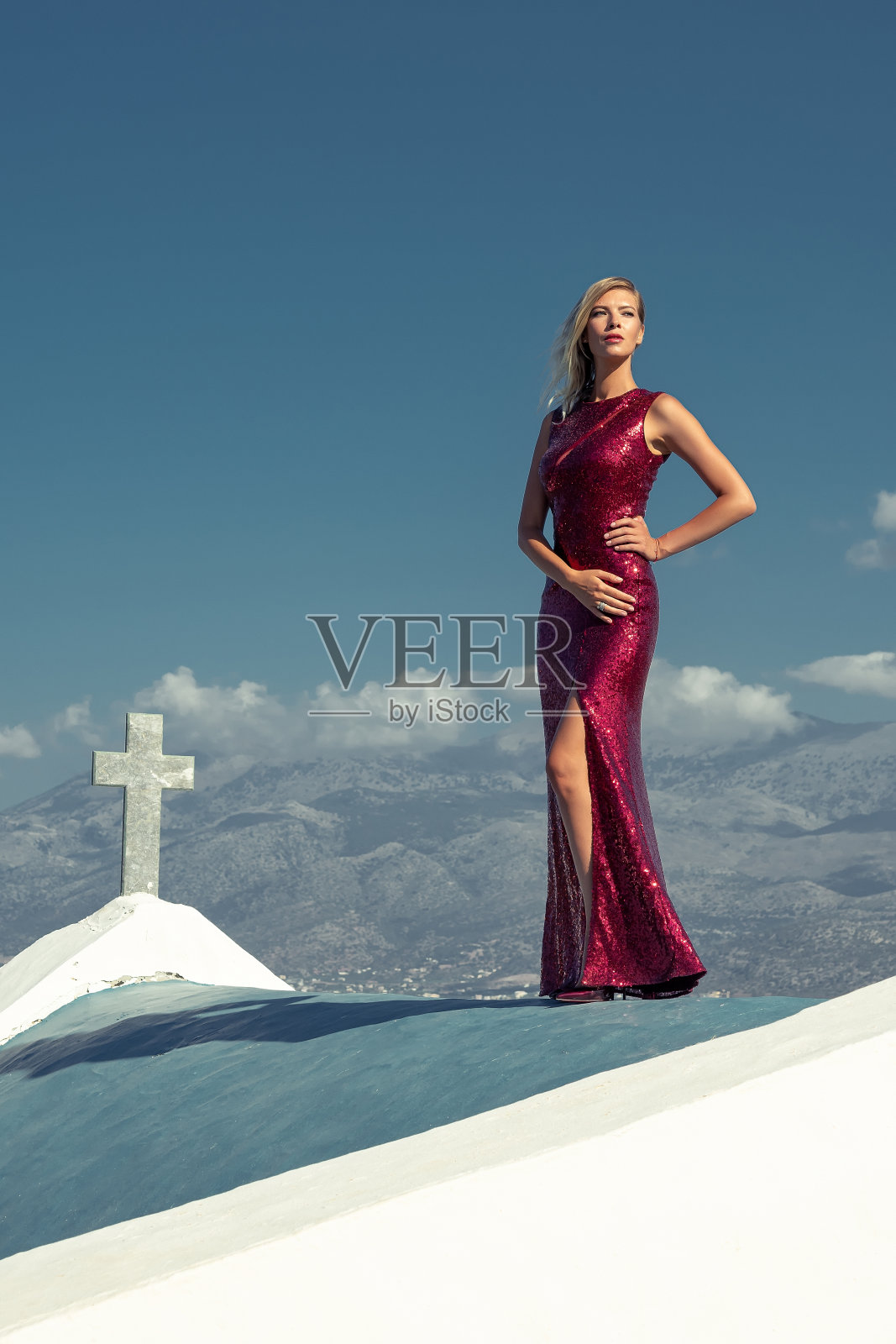 漂亮的年轻女子穿着优雅的红色连衣裙在屋顶摆姿势。时尚的概念。照片摄影图片