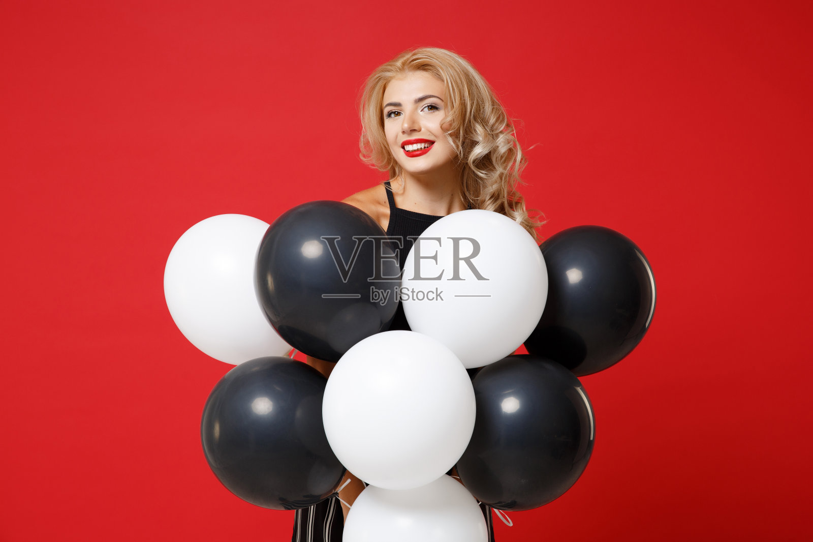 微笑的年轻女子女孩在黑色衣服摆孤立在明亮的红色背景在工作室。情人节生日派对的概念。模拟拷贝空间。庆祝,举着气球。照片摄影图片