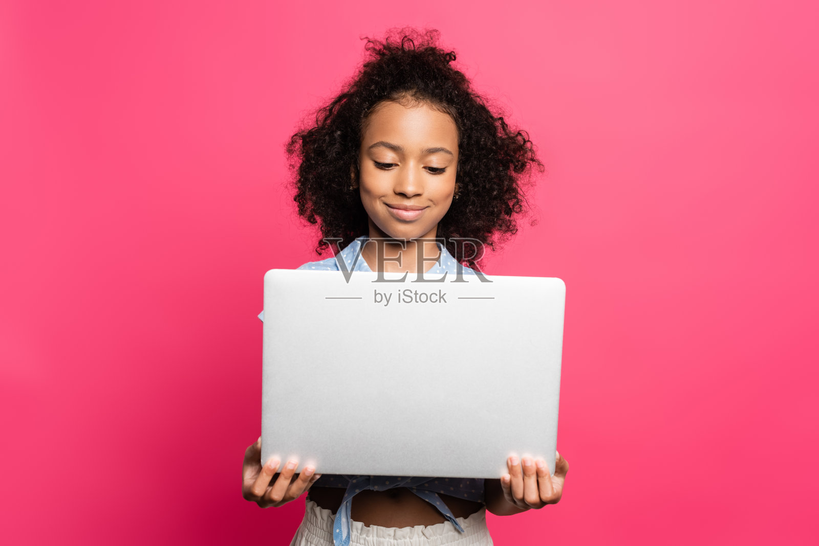 微笑可爱的卷曲的非洲裔美国孩子抱着笔记本电脑孤立的粉红色照片摄影图片